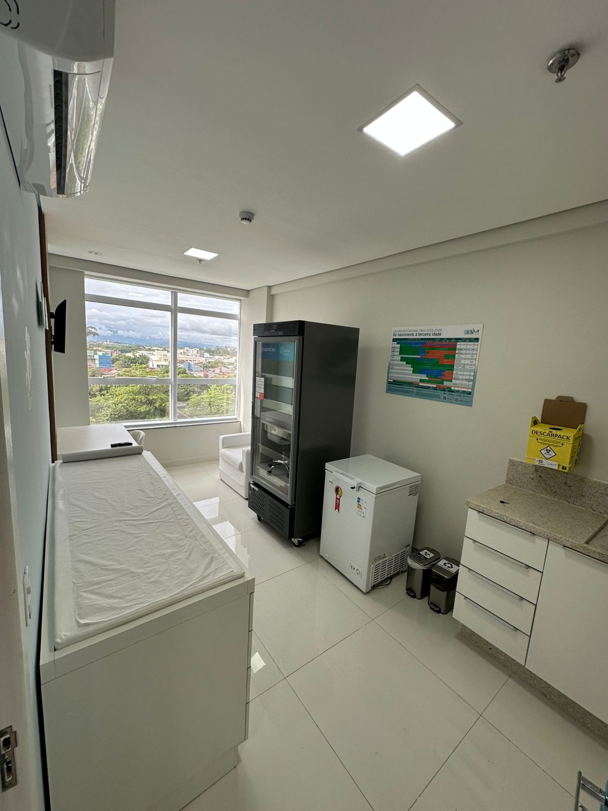 Sala de vacinação com bancada, refrigeradores e vista pela janela